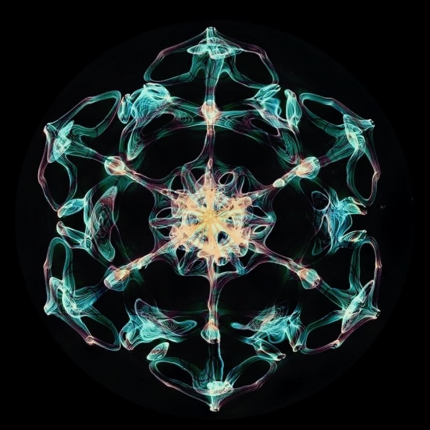 A cymatic pattern — teal and green filaments in perfect symmetry around a golden centre, on black